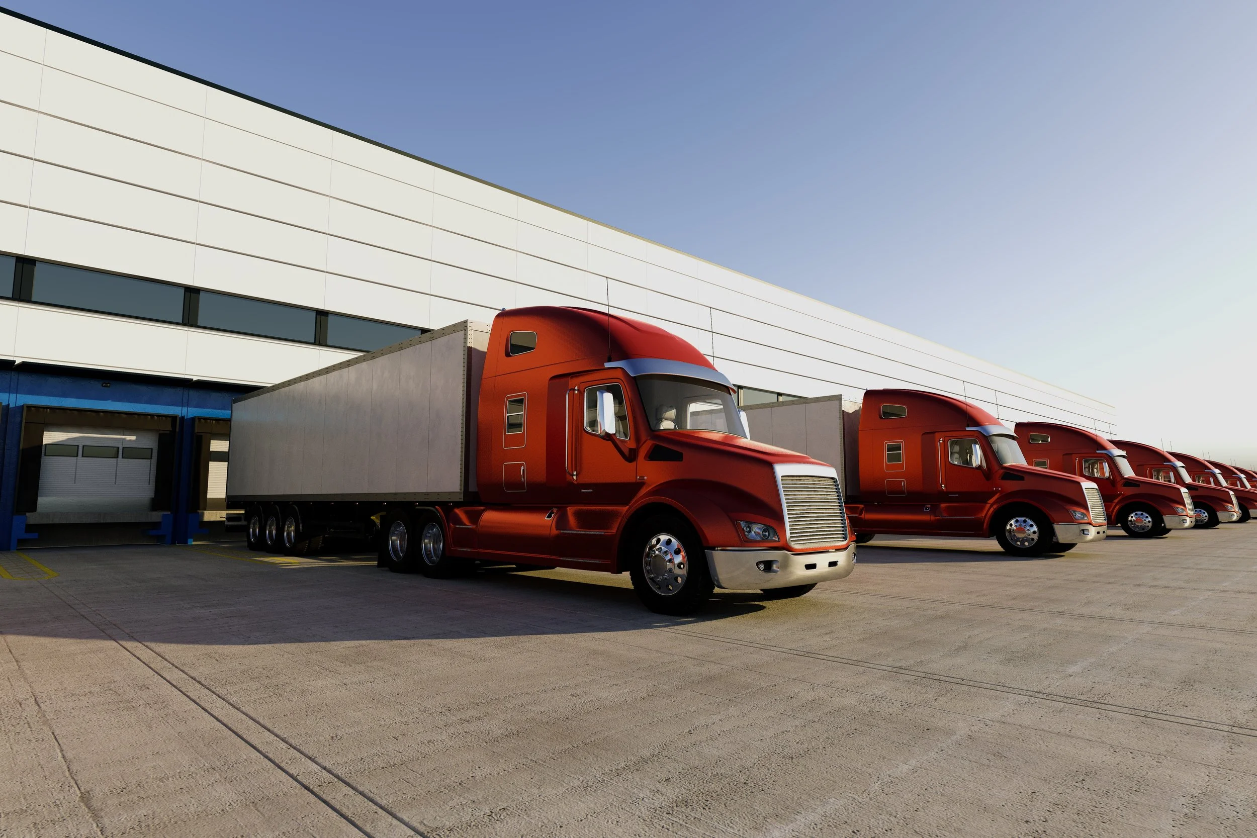 Multiple red semi-truck trailers parked in a line outside a warehouse under a clear sky.