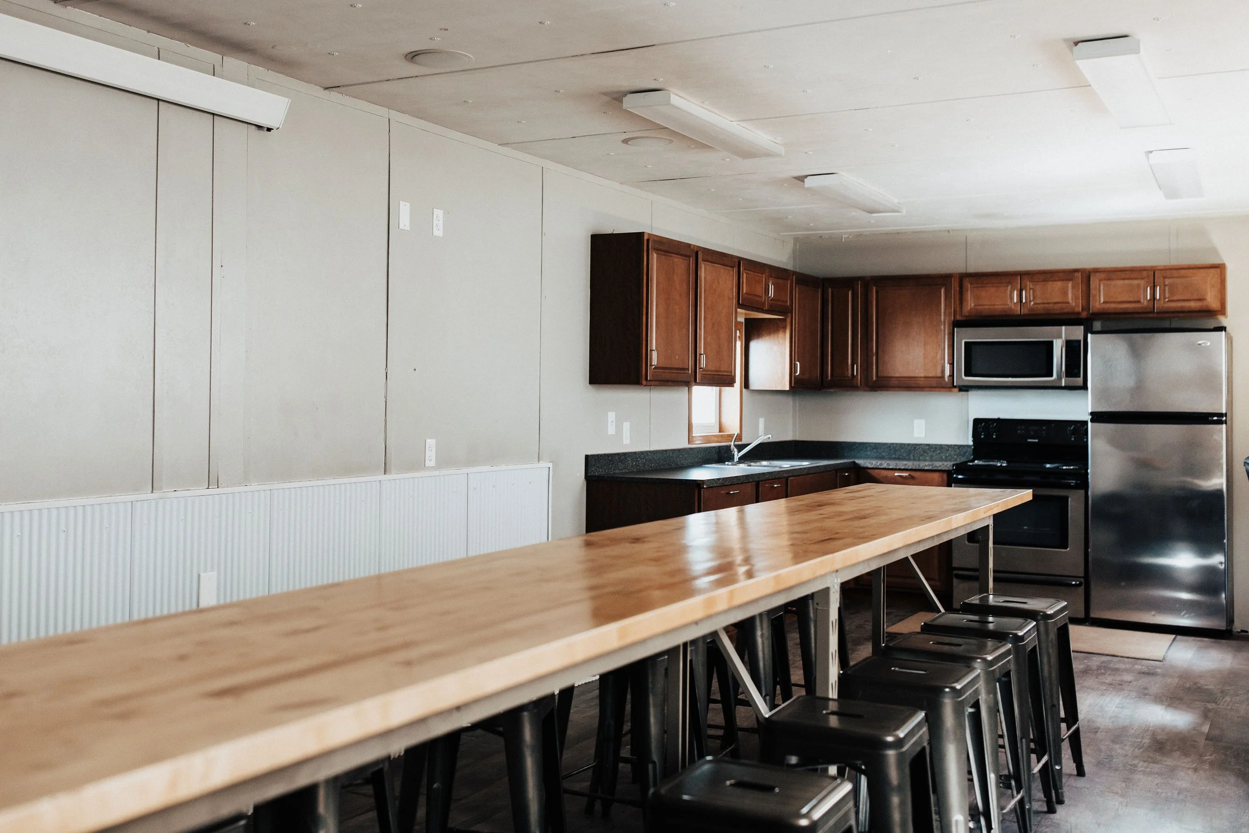 Kitchen with wooden cabinets, black countertops, stainless steel appliances, a wooden bar counter, and black stools.