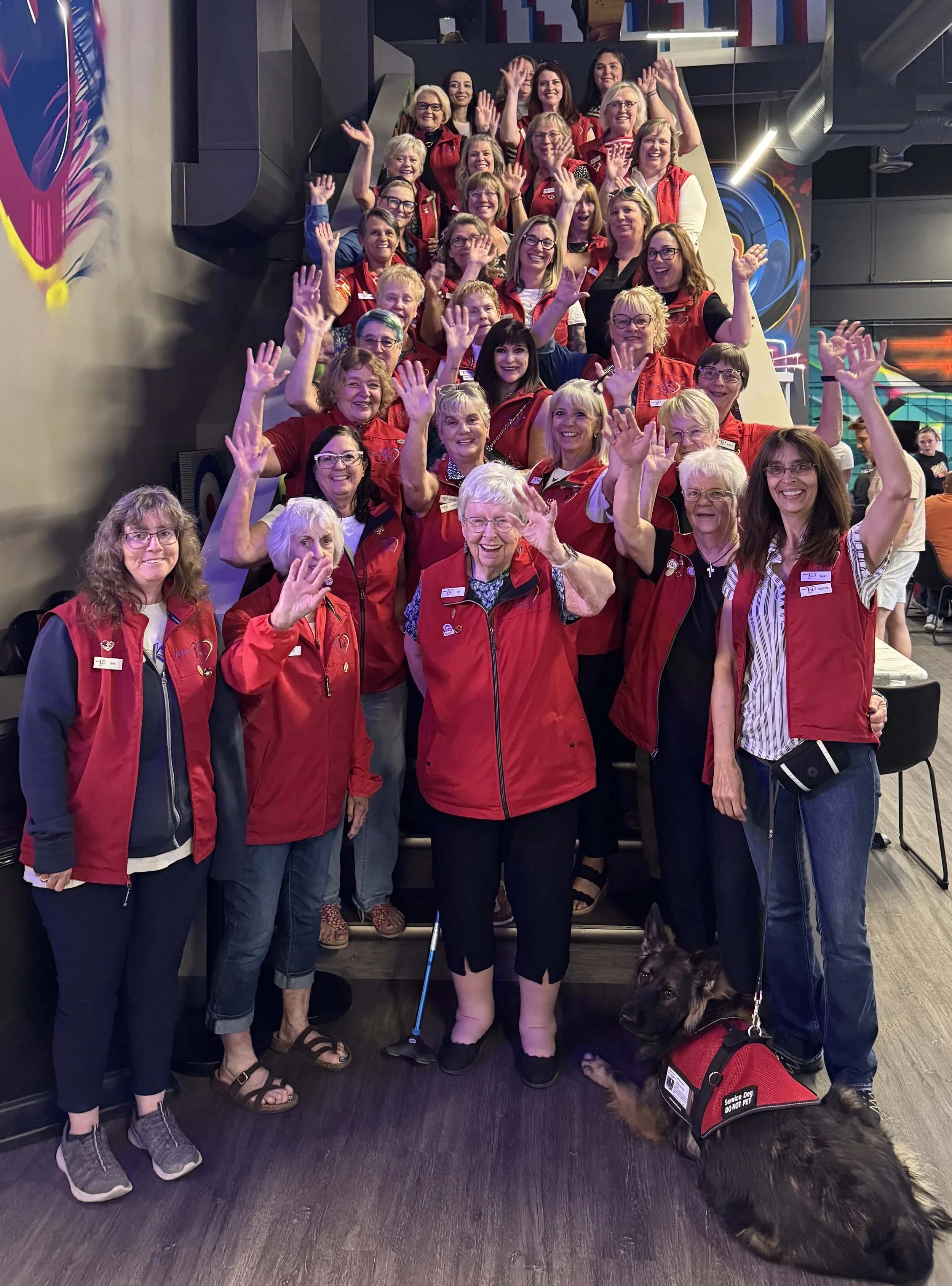 A group on women in red vests waving and smiling at the camera