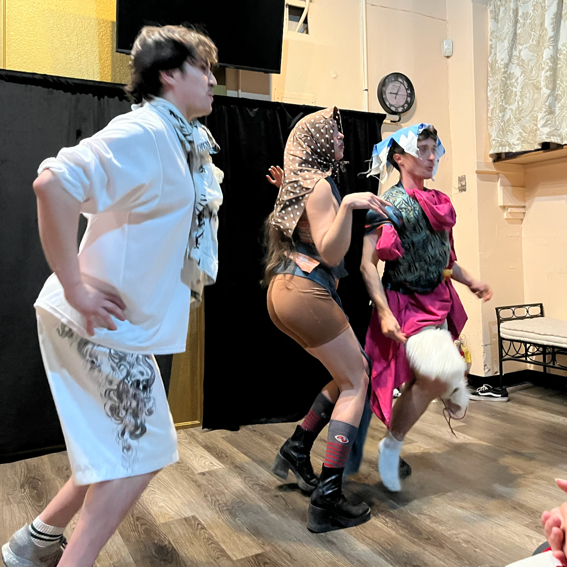 People dressed in colorful costumes engaged in a theatrical performance, with one person holding a stuffed animal.