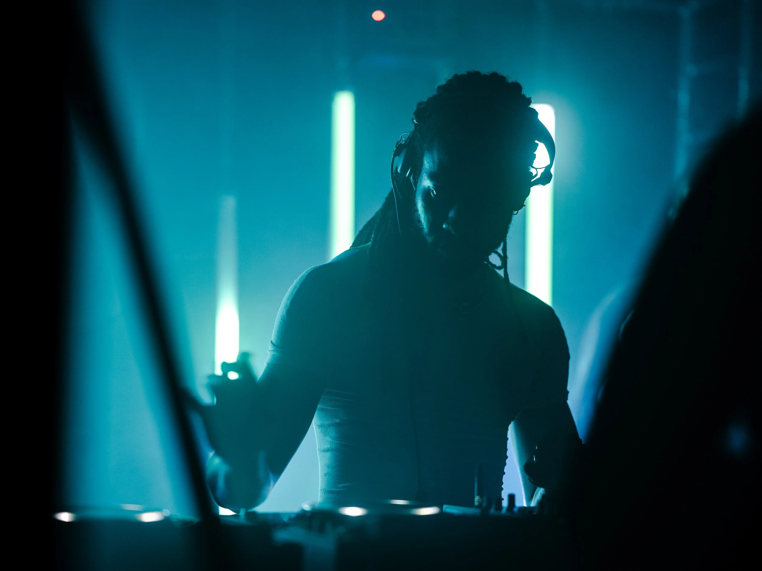 Silhouette of a DJ with headphones, possibly performing, with neon lights in the background.