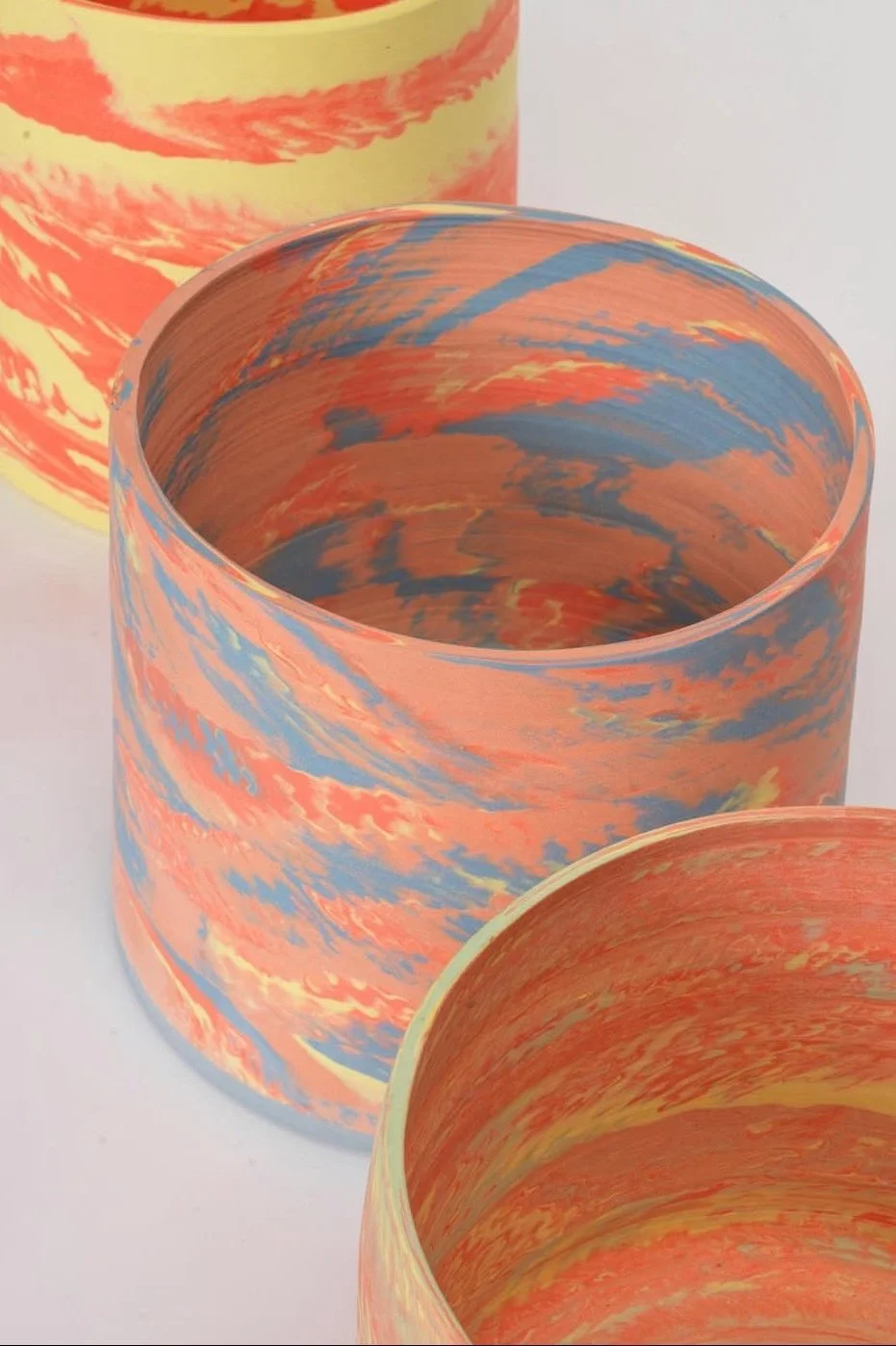 Colorful cylindrical pottery with an abstract marbled design in orange, blue, yellow, and red hues.