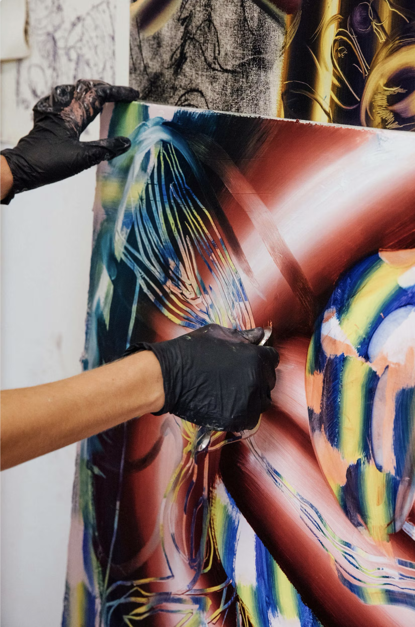 Artist wearing black gloves working on a colorful abstract painting with vivid lines and shapes.