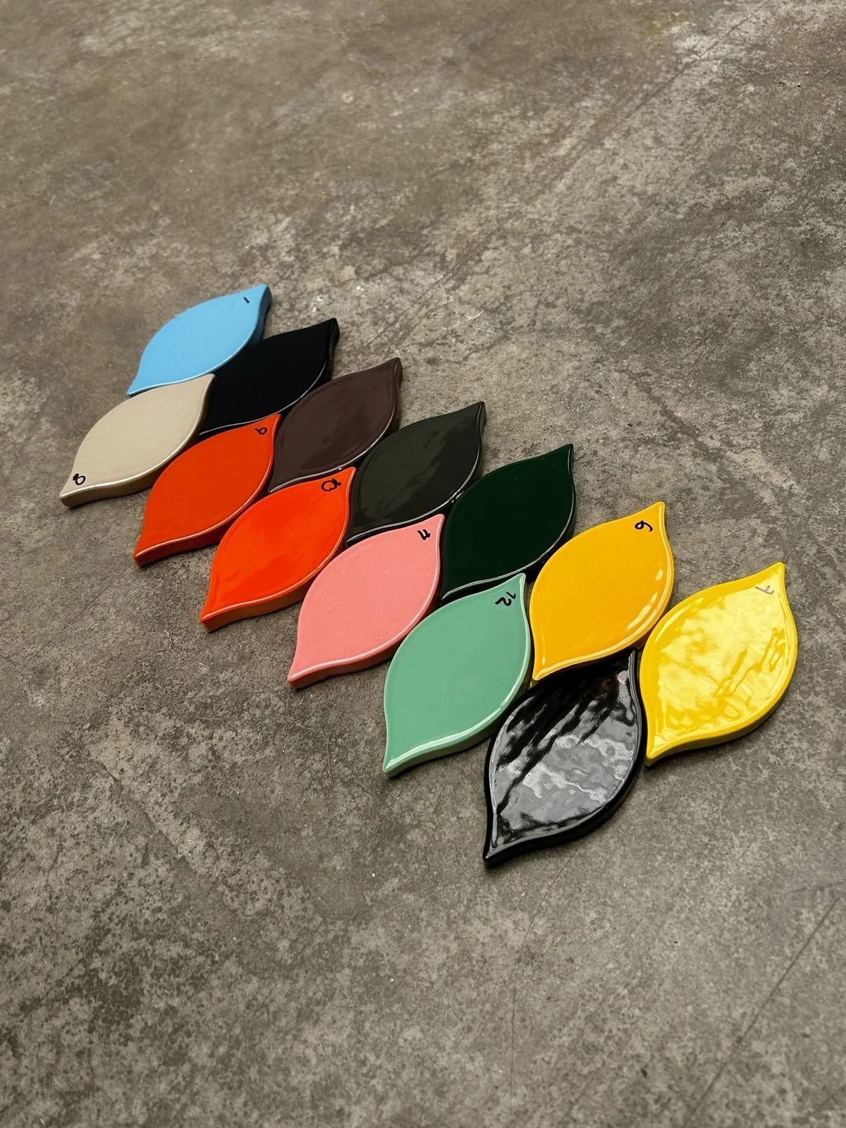 Colorful leaf-shaped ceramic tiles arranged in a pattern on a concrete surface.