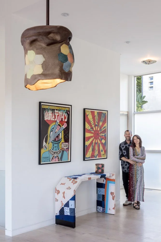 Modern interior with colorful artwork on the walls, a unique pendant light, a patterned console table, and two people standing and smiling.