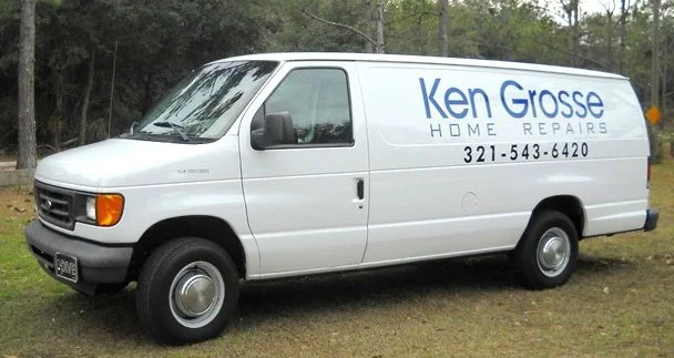 White van with blue text advertising Ken Grosse Home Repairs, including a phone number, parked on grass with trees in the background.