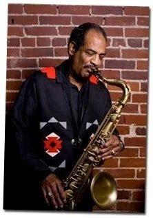 Marshall Petty, President of the Charleston, WV Blues Society, playing saxophone against a brick wall.
