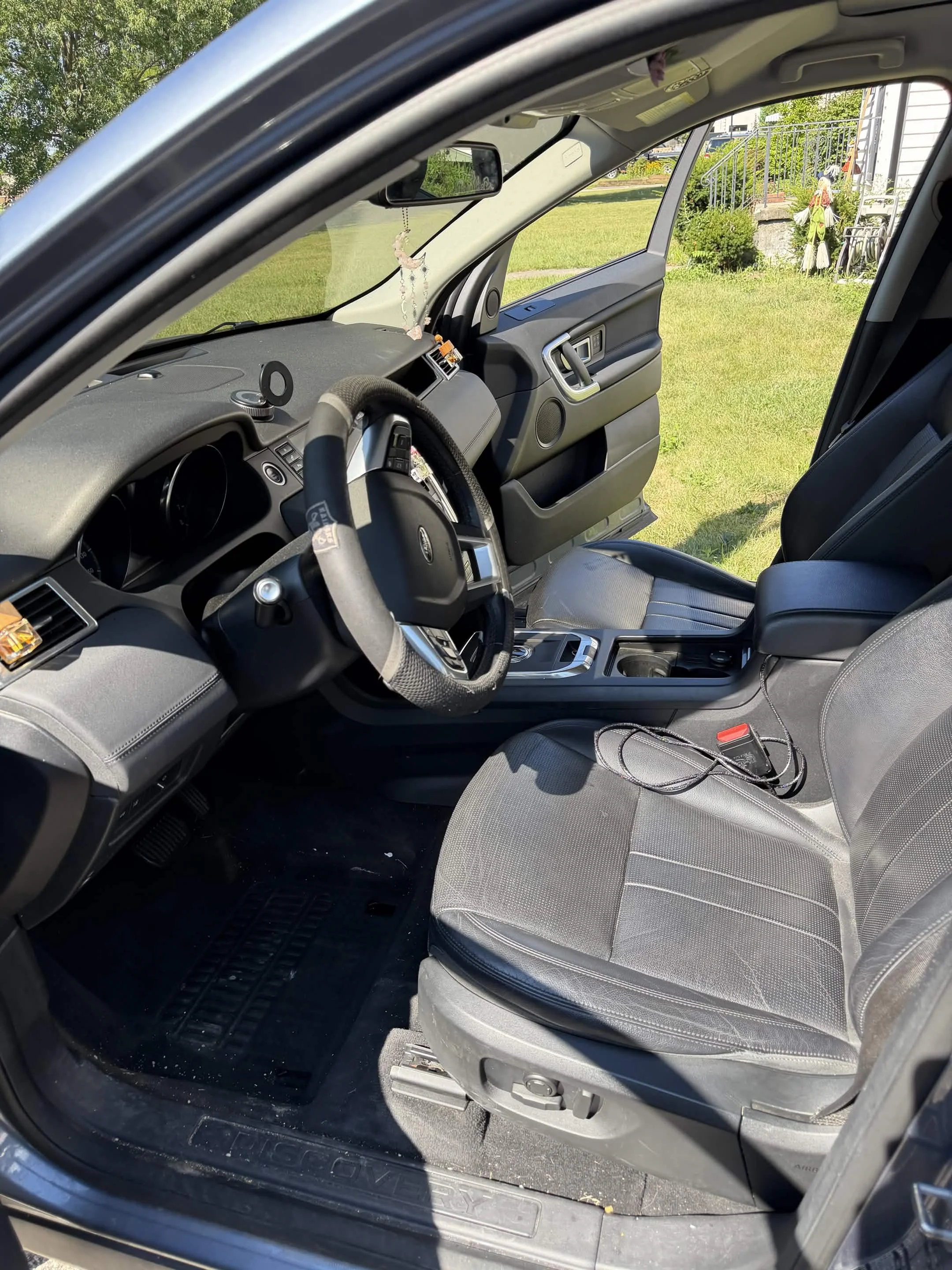 The interior of a vehicle showing the passenger seat, dashboard, steering wheel, and center console, with a view of a grassy yard and house outside.