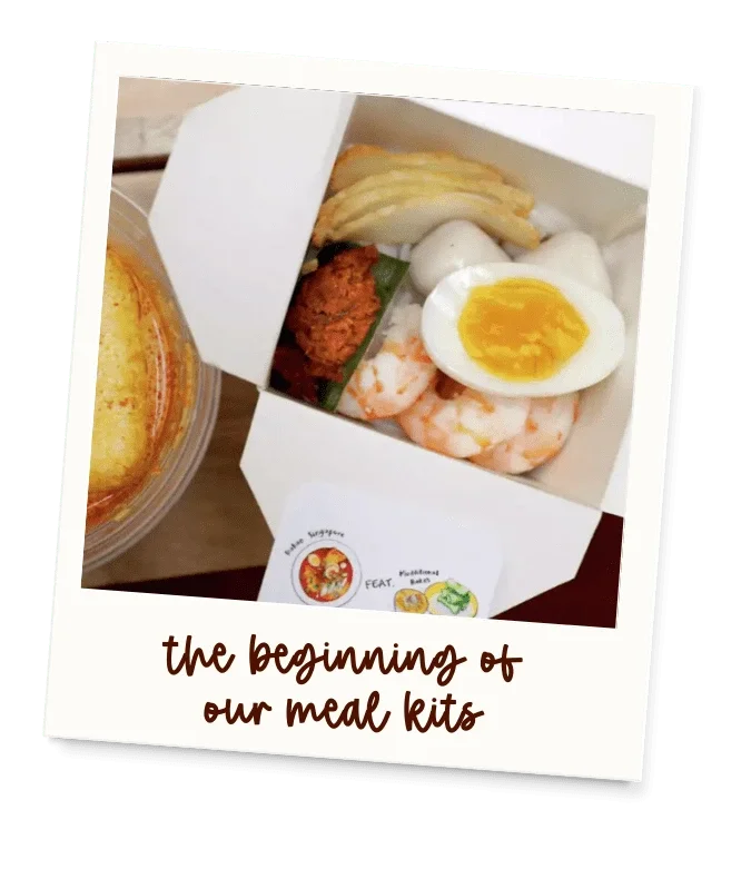 A photo of an open meal kit box containing shrimp, half a boiled egg, potato chips, and fried chicken pieces. The photo is tilted and overlaid with text that says 'the beginning of our meal kits.'