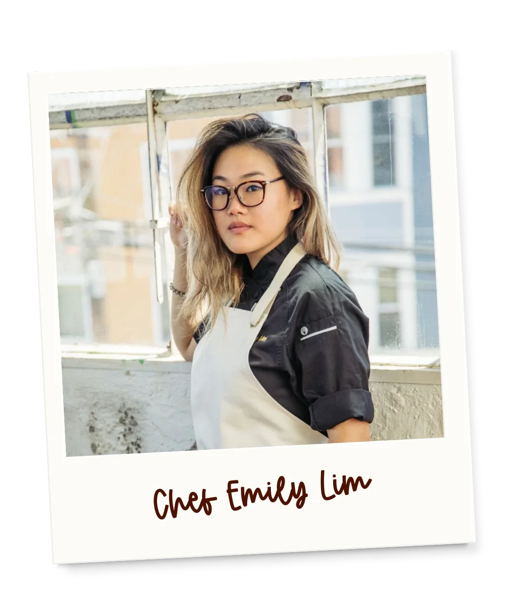 A woman with glasses and wavy hair standing in front of a window, wearing a black shirt and white apron, with the caption 'Chef Emily Lim'.