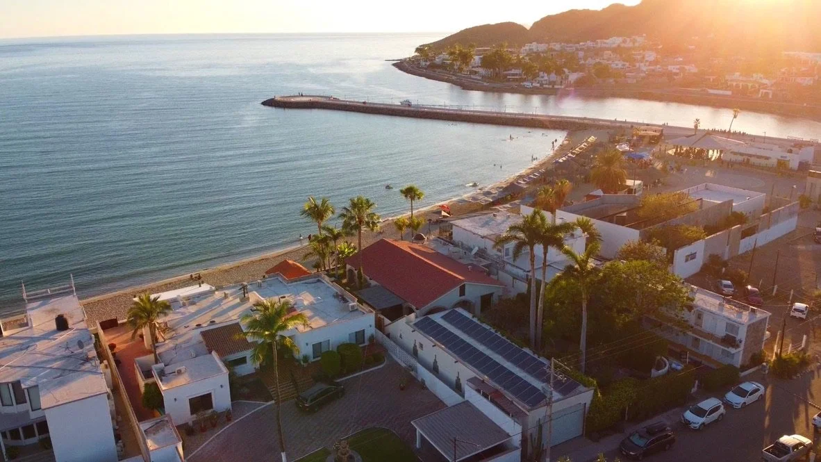 Aerial sunset view of the coastal Miramar neighborhood with houses, palm trees, and a beach near the ocean at sunset. Calm waters and a gorgeous sand beach make this one of the most active and inviting neighborhoods in all of San Carlos or Guaymas.