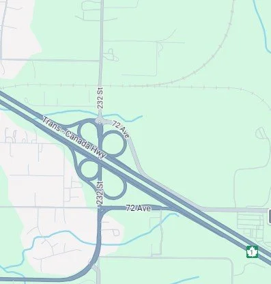 Map showing a highway interchange with loops and ramps, including Trans-Canada Hwy, 72 Ave, and 223 St, surrounded by green areas and some water bodies.