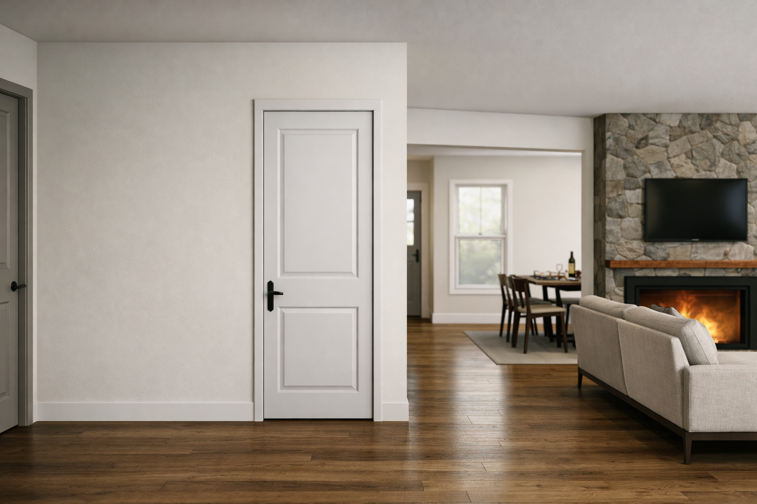Interior of a living room with white walls and wood flooring, showing a closed white door, part of a stone fireplace with a mounted TV, a beige sofa, a dining table with chairs, and a window with natural light.
