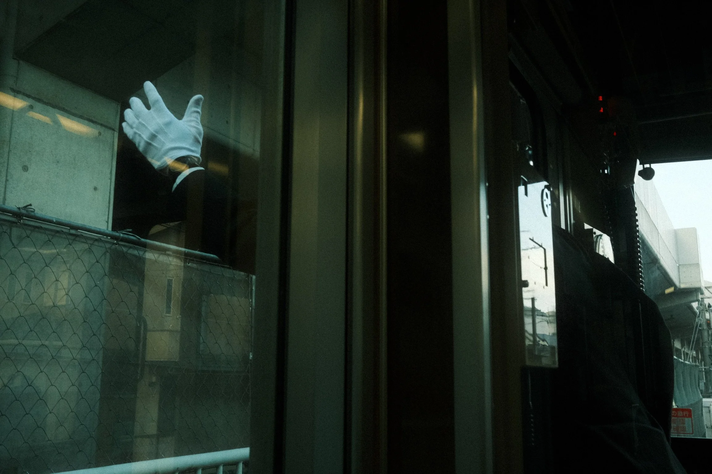 Reflected image of a person wearing gloves, viewed through a glass window at a city street scene during daytime.