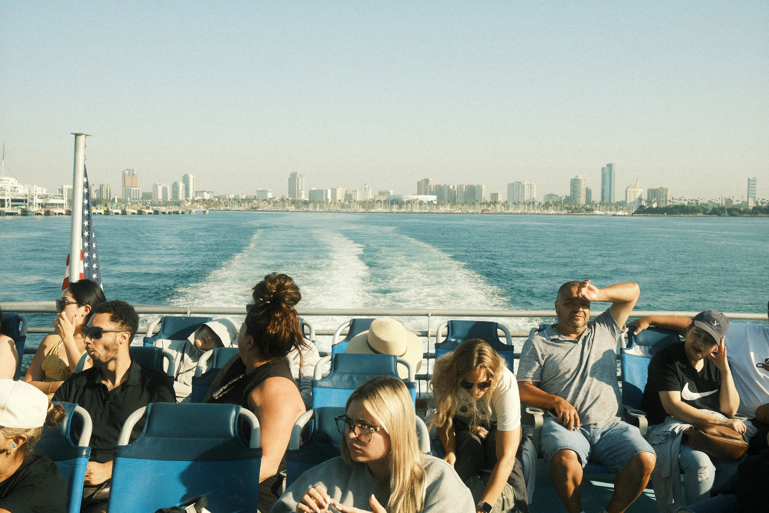 People sitting and relaxing on a boat ride across the water with a city skyline in the background.