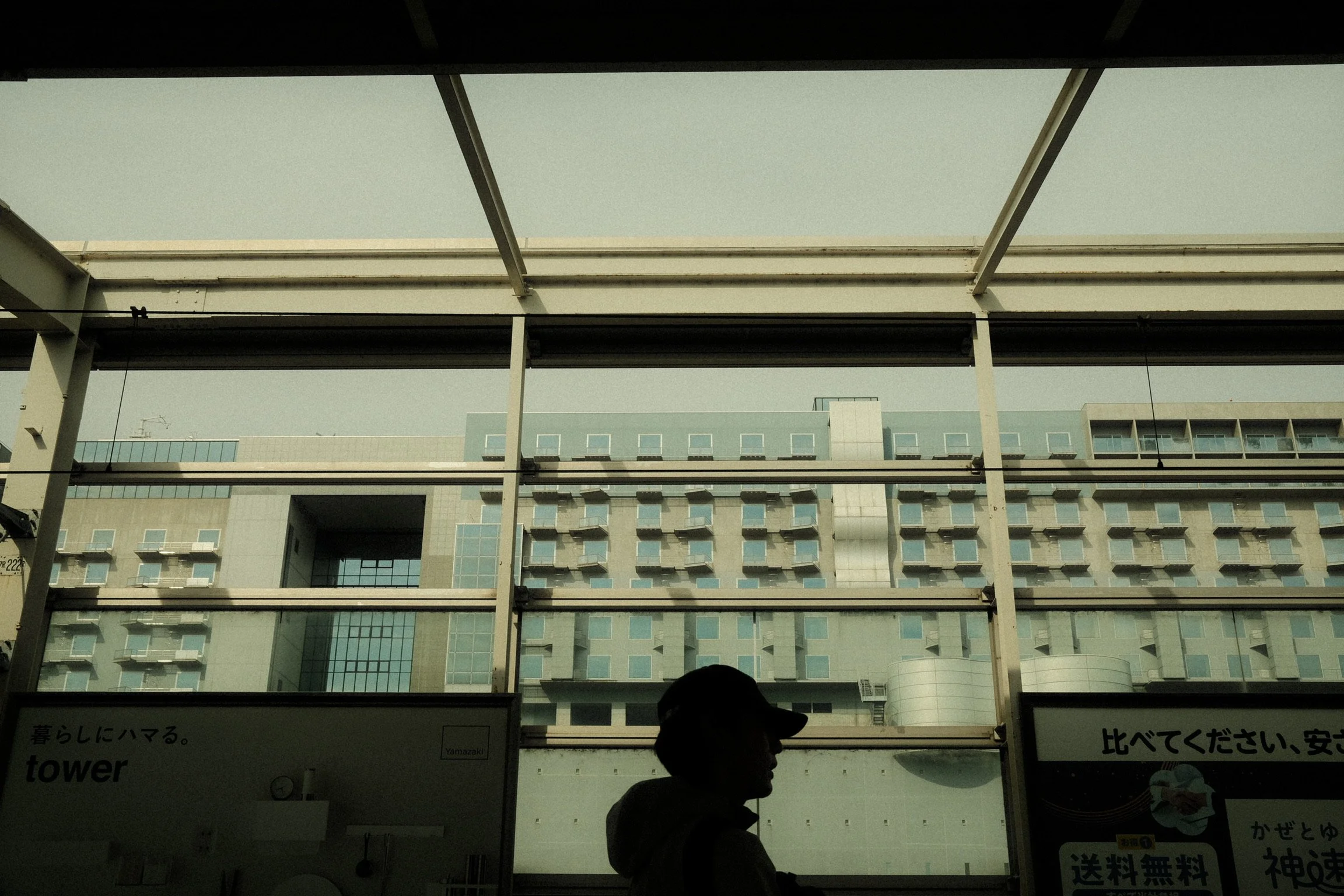 Interior view of a building with large windows revealing multiple residential or hotel rooms and a person wearing a hat sitting or standing inside.