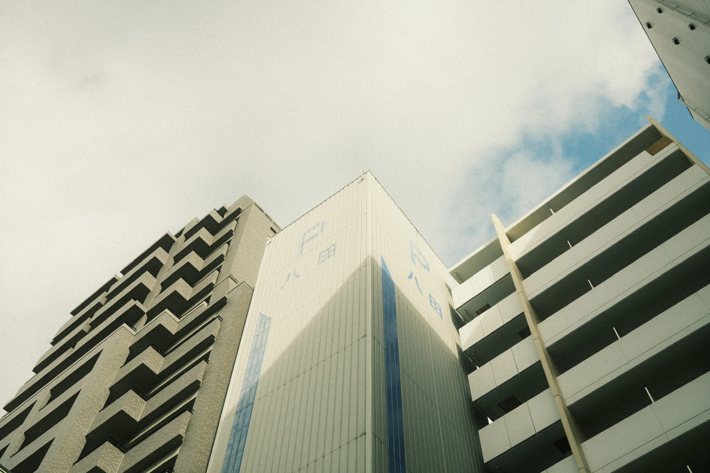 View of modern high-rise buildings from below, with blue sky and clouds in the background.
