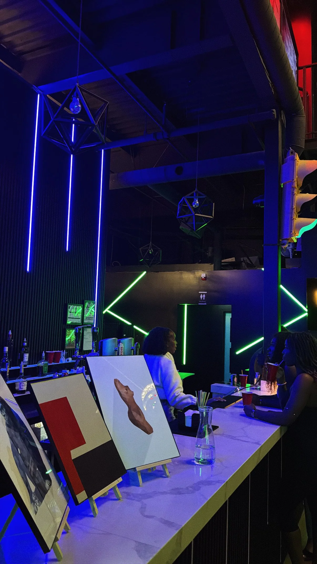 Paintings displayed under blue neon lights at a Toronto paint and sip night.
