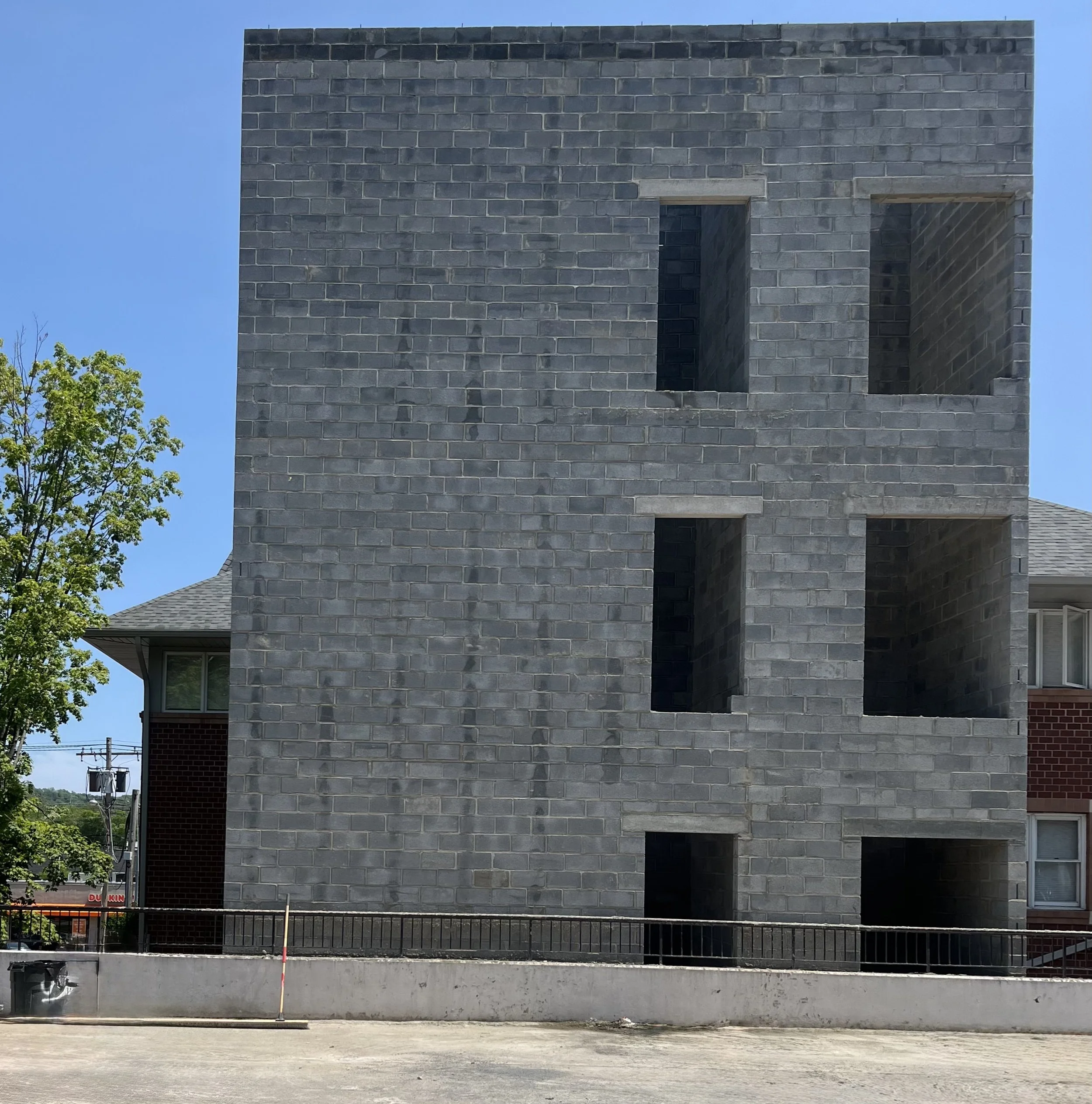 A building under construction with a gray brick exterior and two open window spaces, with a clear blue sky in the background.