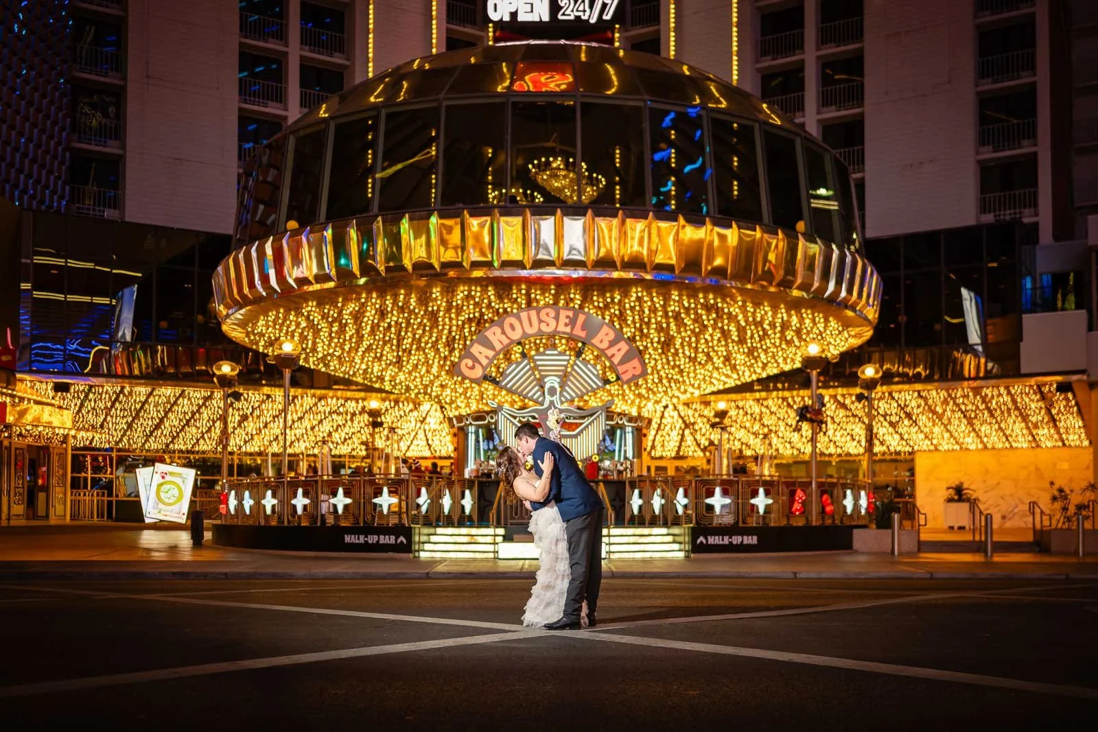 A newlywed couple kissing in front of a brightly lit hotel on a Fremont Street, downtown Las Vegas.