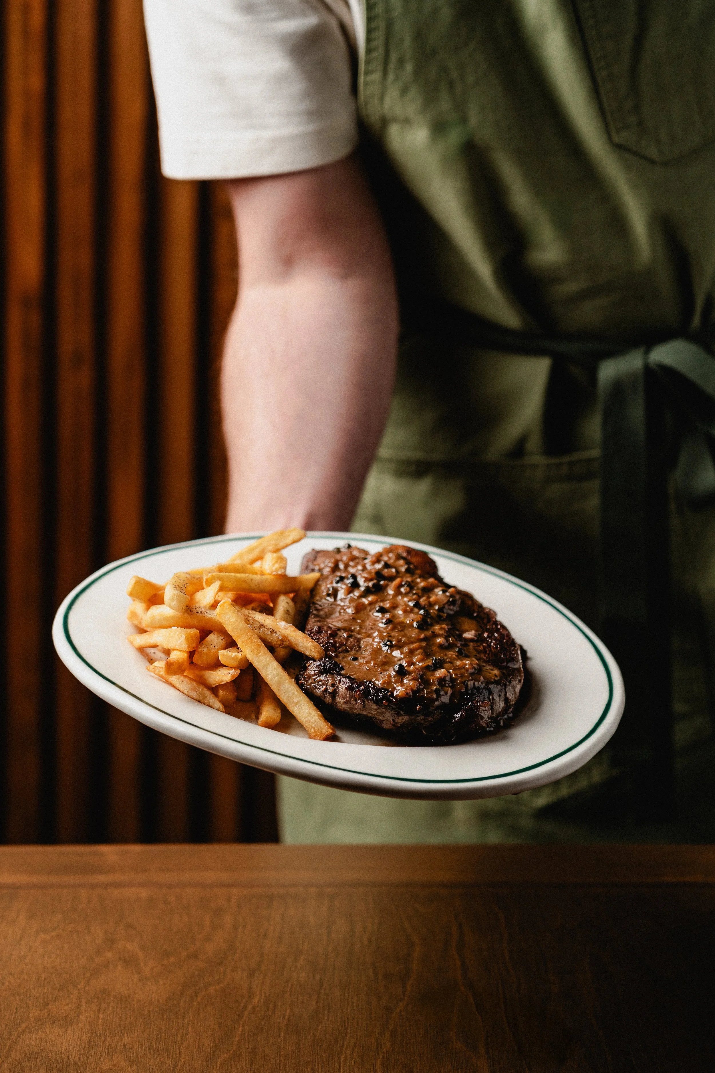 Persona sirviendo un plato con carne asada y papas fritas en un restaurante.