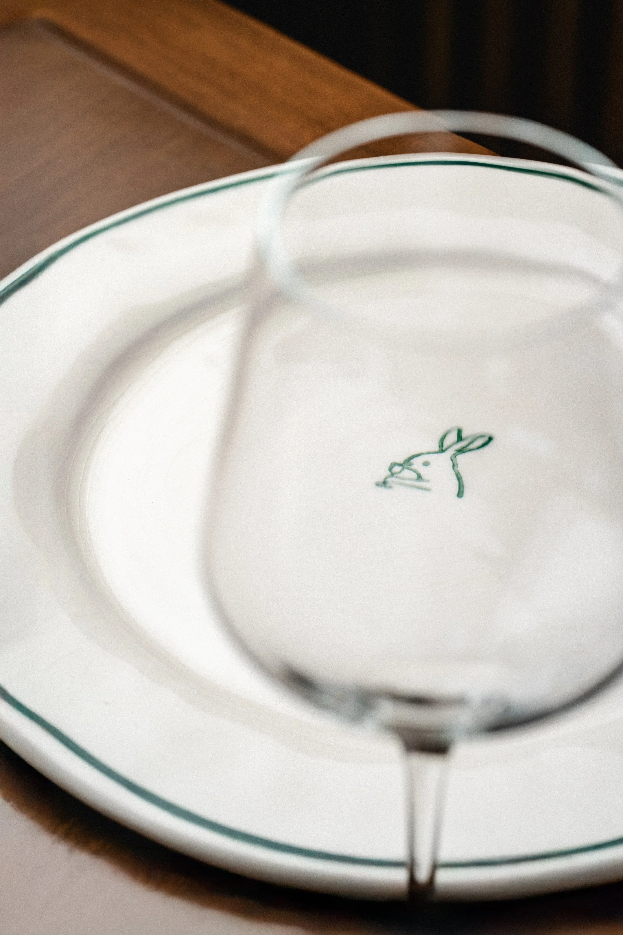 Plato blanco con borde verde, con un tazón de cristal transparente en el centro, sobre una pata de pie, con un dibujo de conejo en la base del plato.