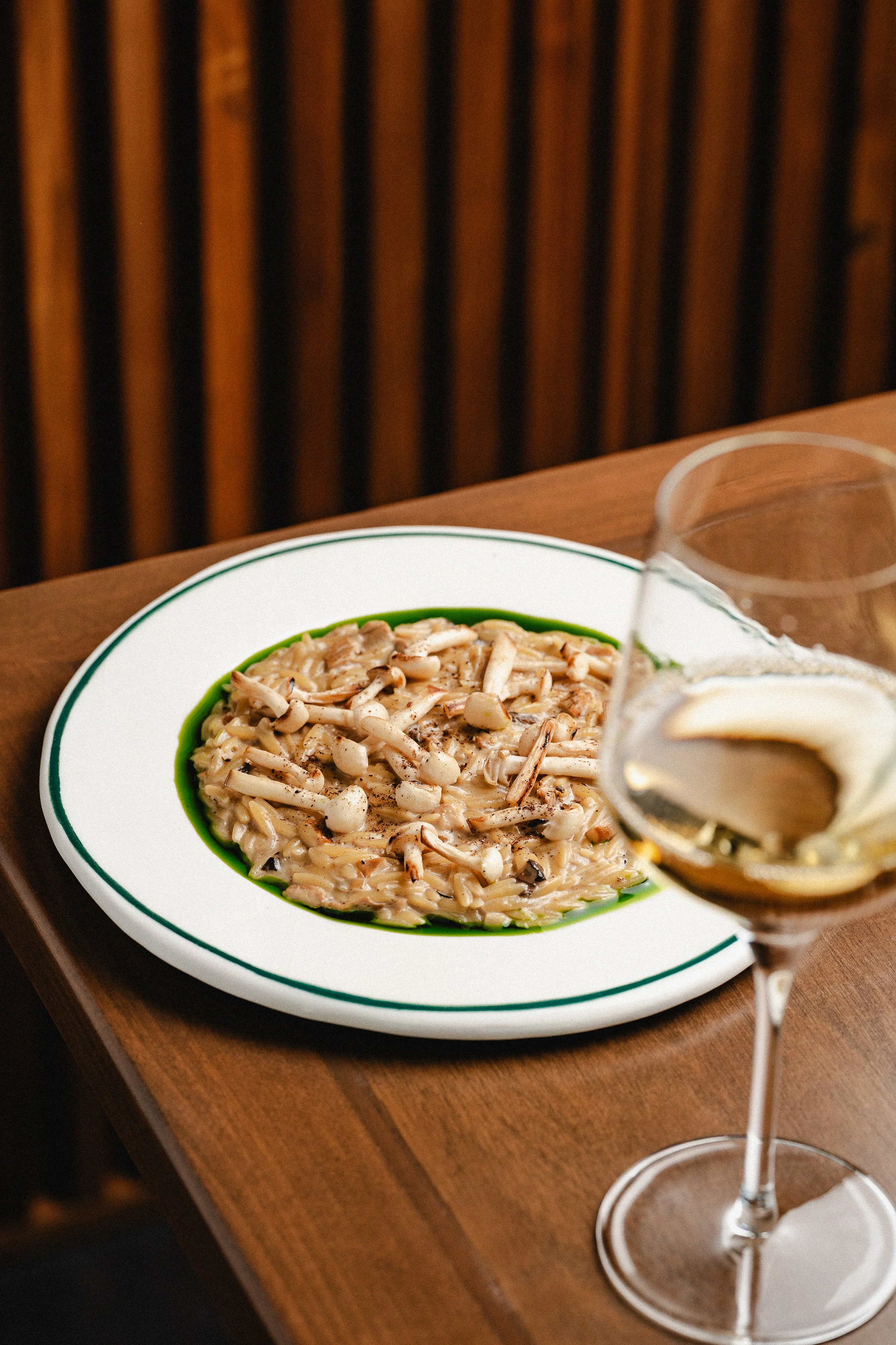 Plato de pasta con hongos y salsa, acompañado de una copa de vino con una rodaja de limón.