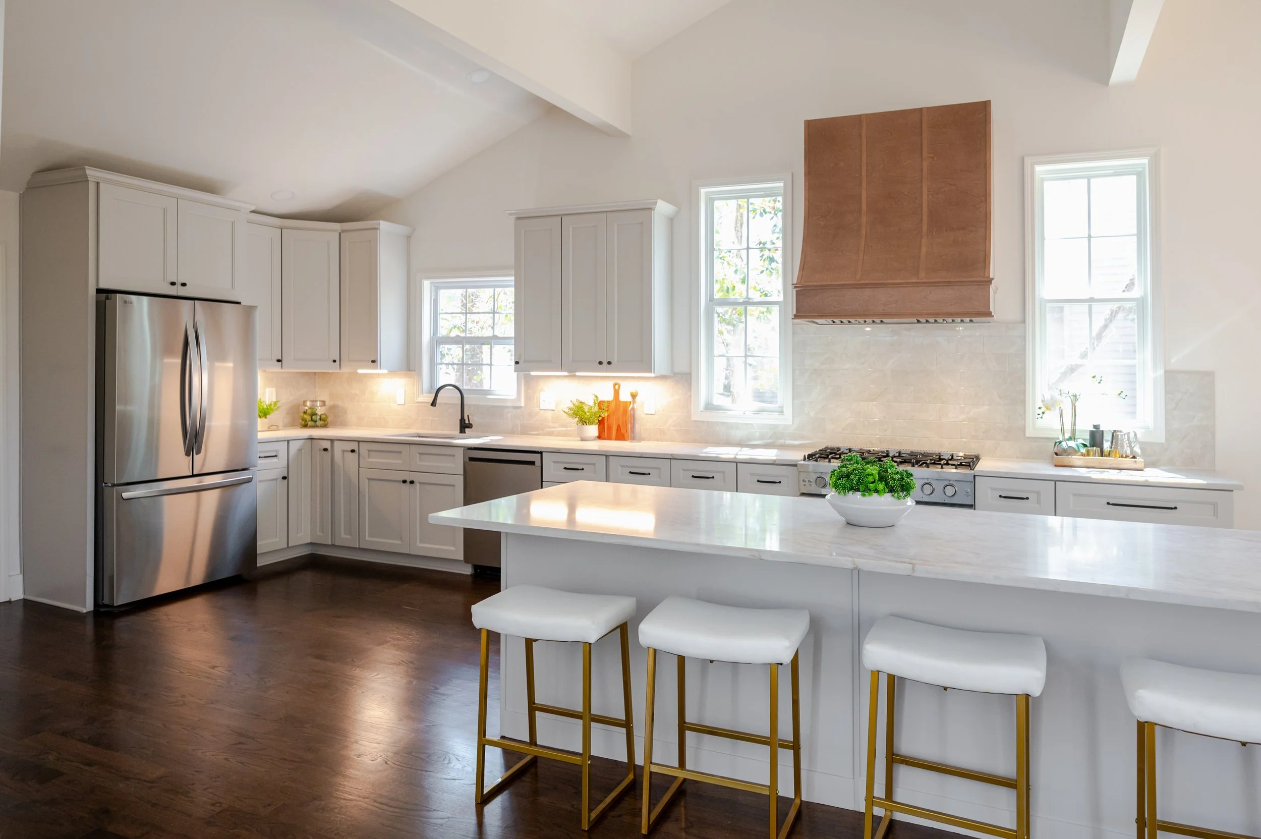 Spacious open-concept living room with wood-beamed ceilings, white sofas, modern art, and a stone fireplace with large windows letting in natural light.