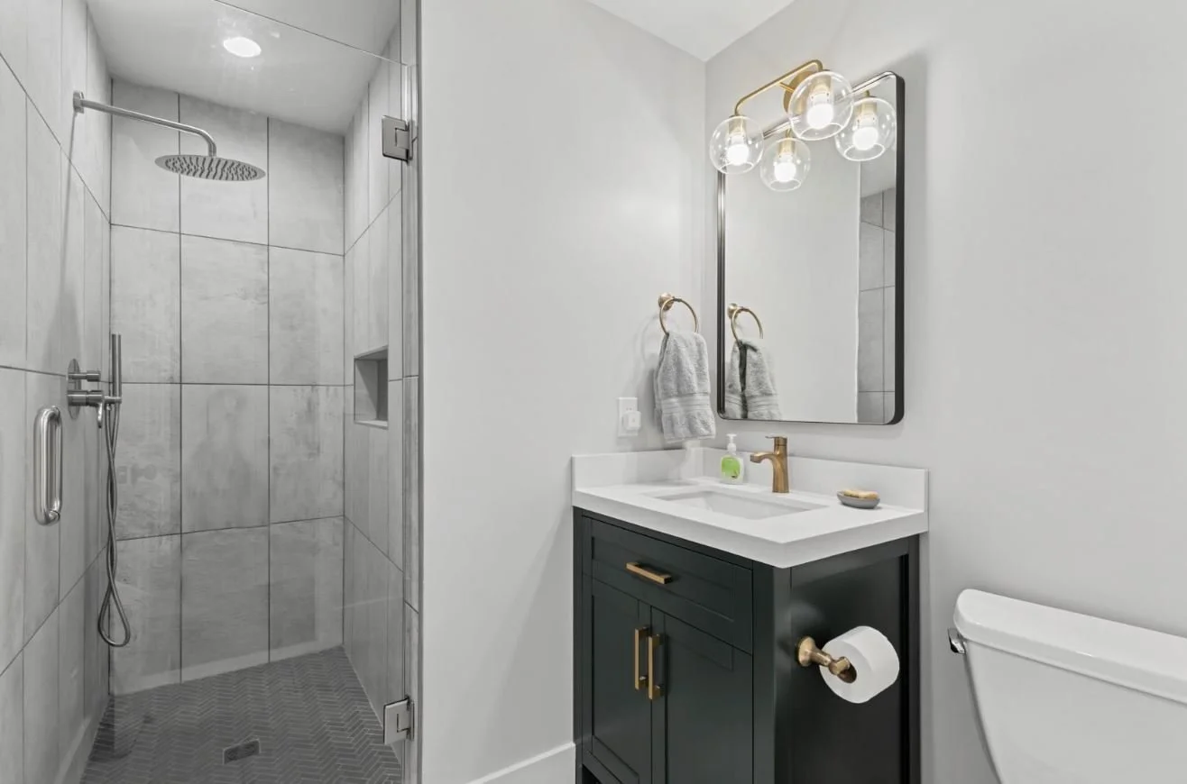 Modern bathroom with a walk-in shower, vanity with gold fixtures, mirror, and toilet.