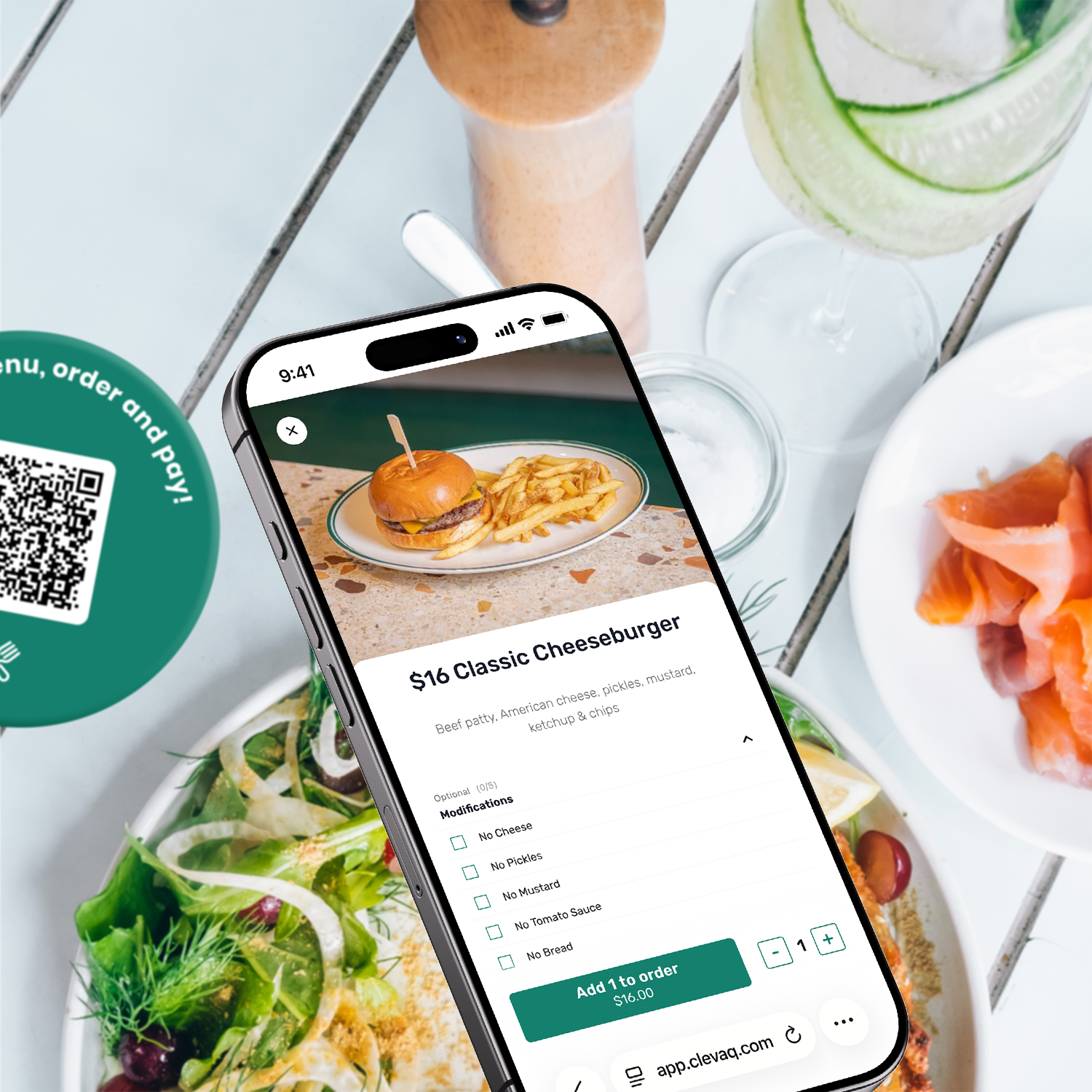 Smartphone displaying a menu for a cheeseburger with options for modifications, surrounded by plates of salad, smoked salmon, a drink with cucumber slices, a salt grinder, and a QR code at a dining table.