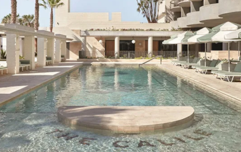 Luxury resort swimming pool with lounge chairs and umbrellas, surrounded by modern architecture and palm trees.