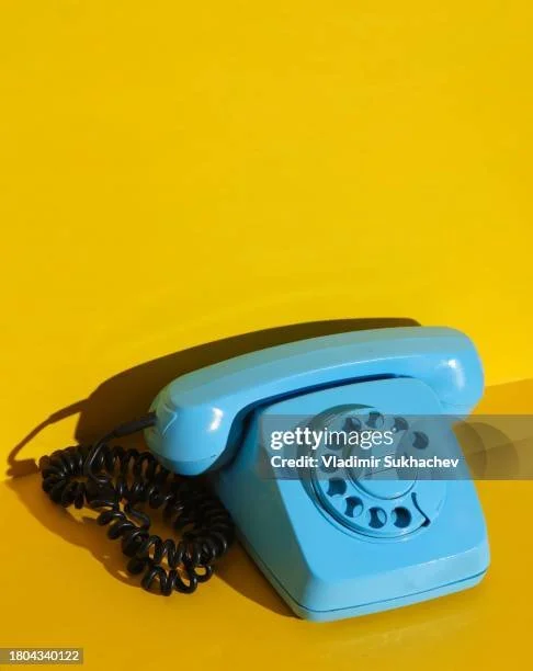 A vintage blue rotary telephone on a yellow background.