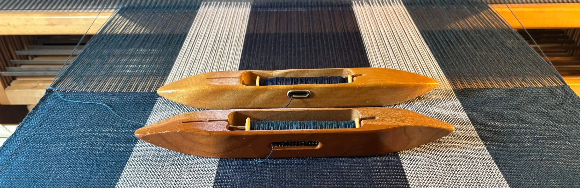 Handwoven blue and white striped fabric on a floor loom with two boat shuttles