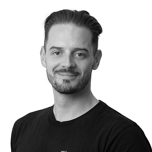 Black and white portrait of a man with styled hair and facial hair, wearing a black T-shirt.