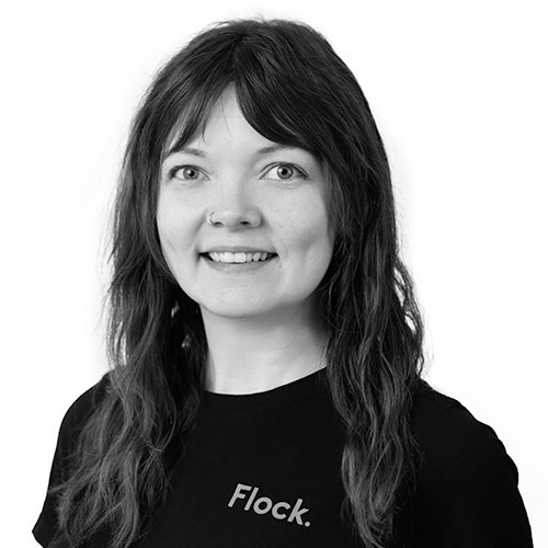 Black and white portrait of a woman with long wavy hair and a nose ring, wearing a black T-shirt that says 'Flock'.