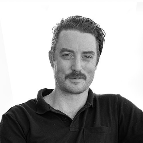 Black and white portrait of a man with styled hair, a mustache, wearing a collared shirt, and looking confidently at the camera.