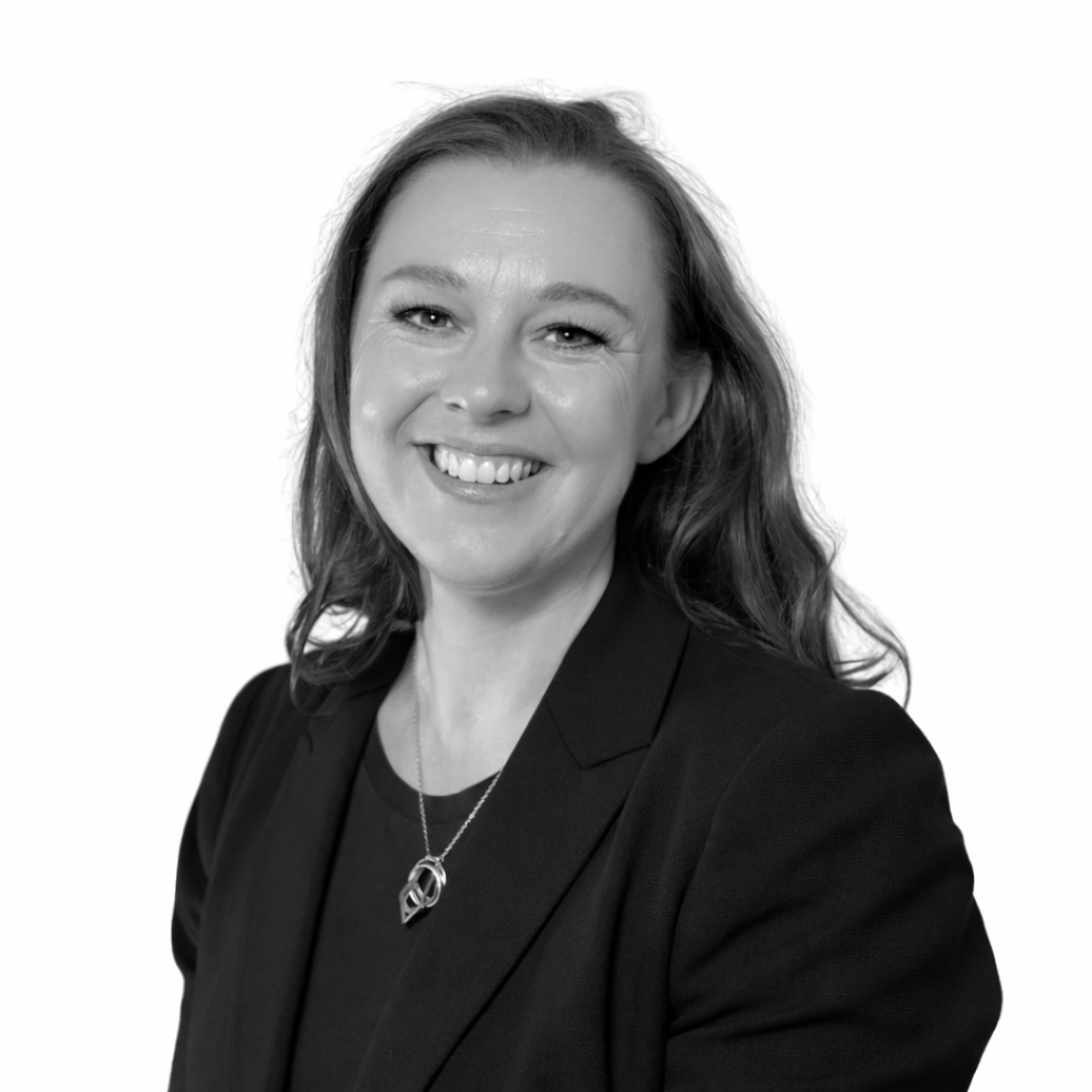 Black and white portrait of a smiling woman with wavy hair, wearing a blazer and a necklace.