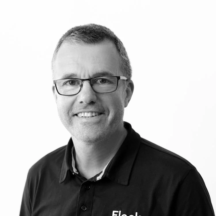 Black and white portrait of a man with glasses, short hair, wearing a collared shirt, smiling at the camera.