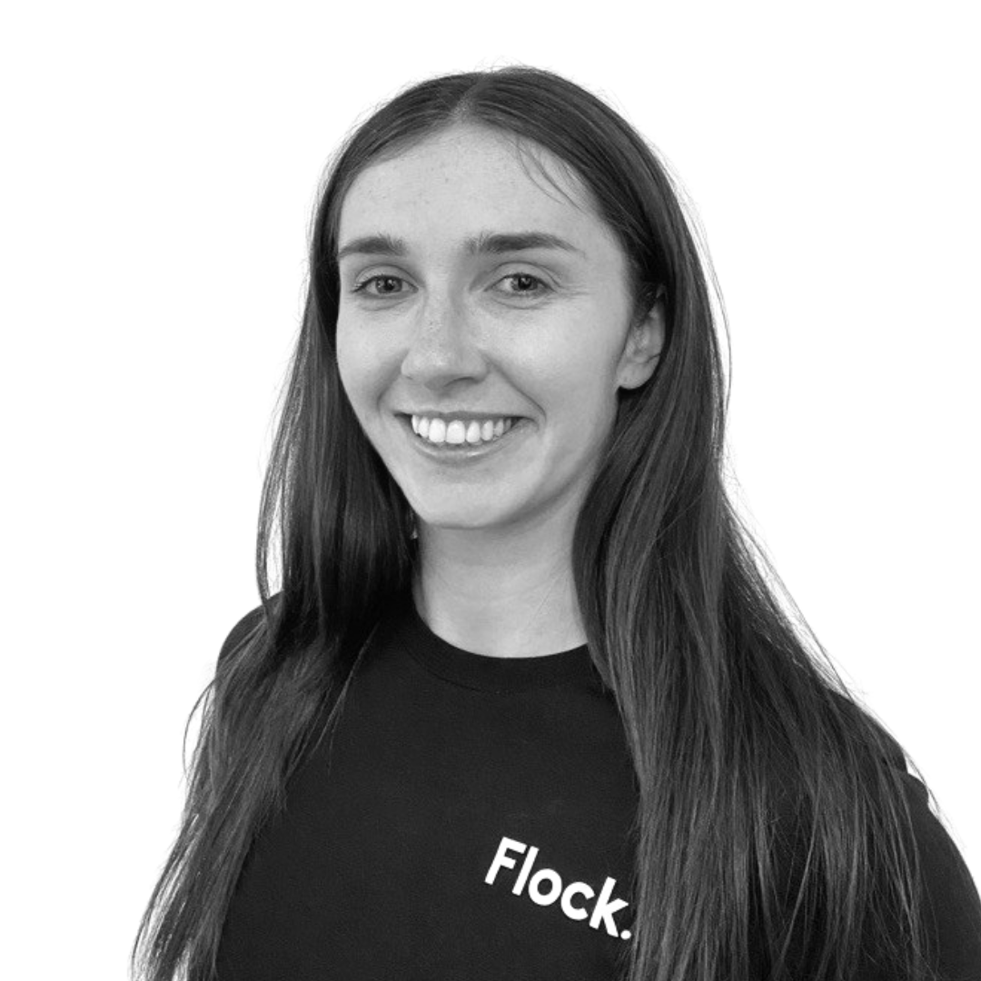 Black and white portrait of a young woman with long hair, smiling, wearing a dark shirt, in front of a plain white background.