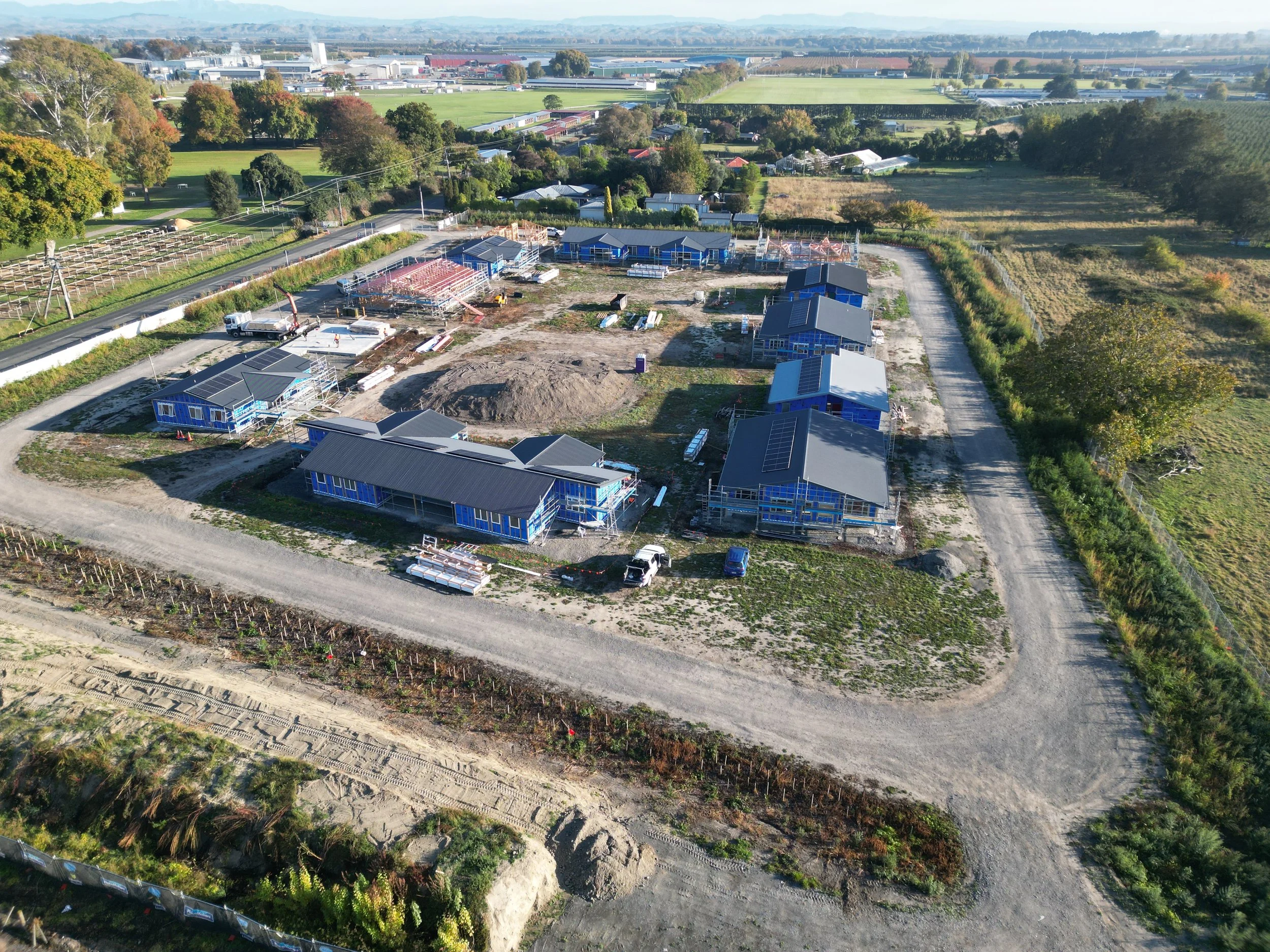 Aerial view of a construction site with several buildings in progress, surrounded by rural landscape and green fields.