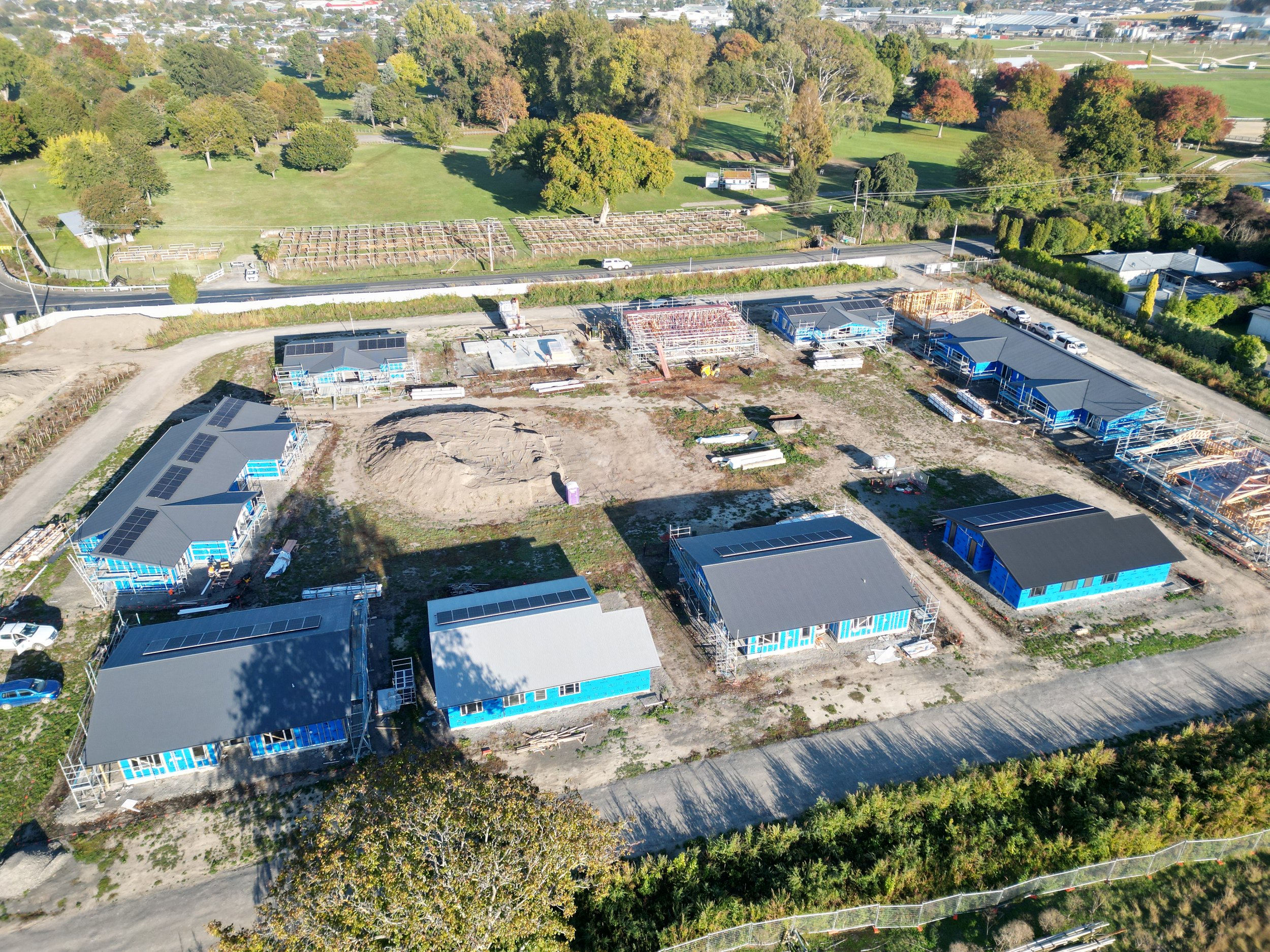 Aerial view of a construction site with several buildings in progress, surrounded by trees and green fields.