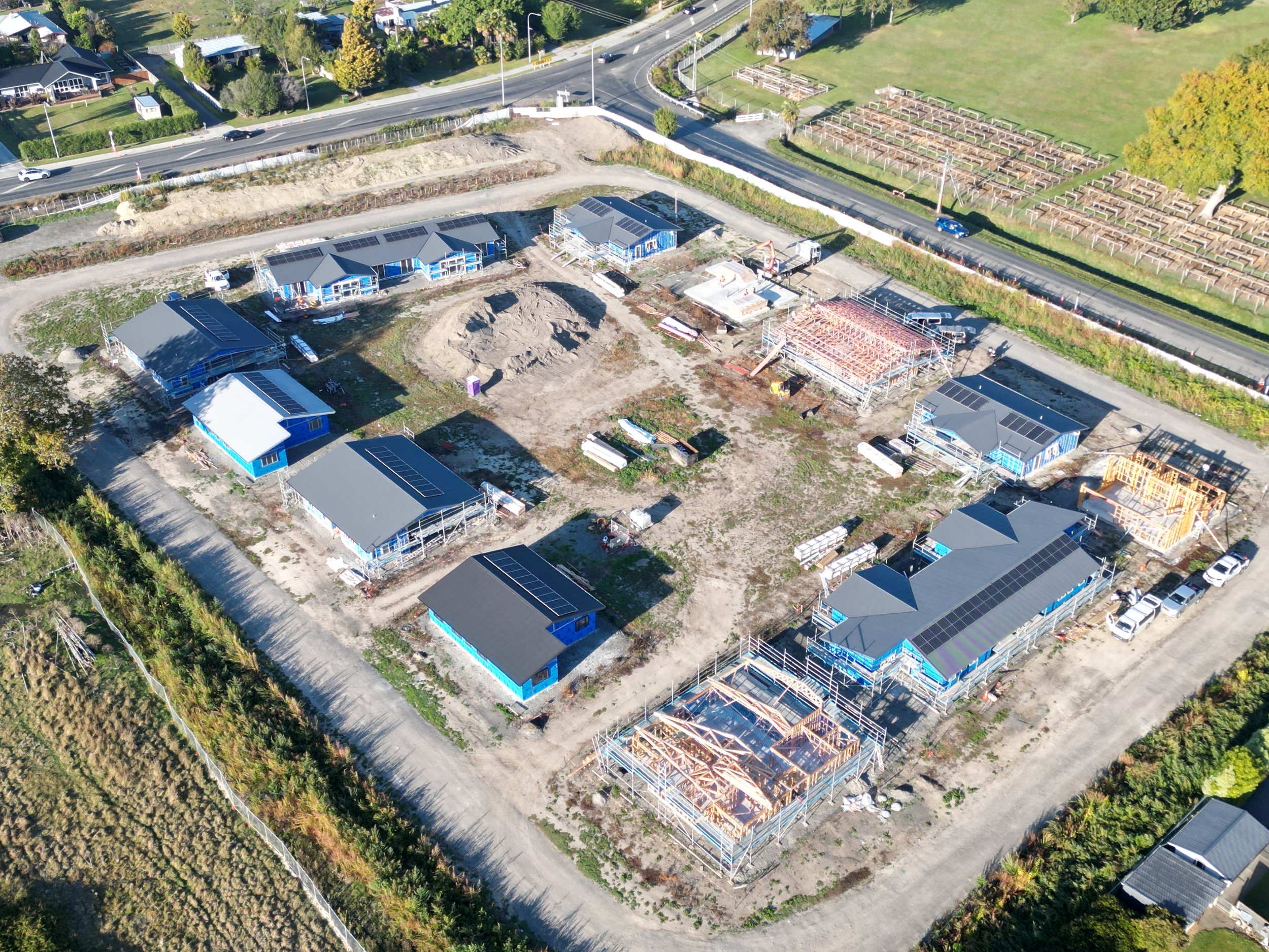 Aerial view of a construction site with multiple buildings under construction, surrounded by roads and greenery.