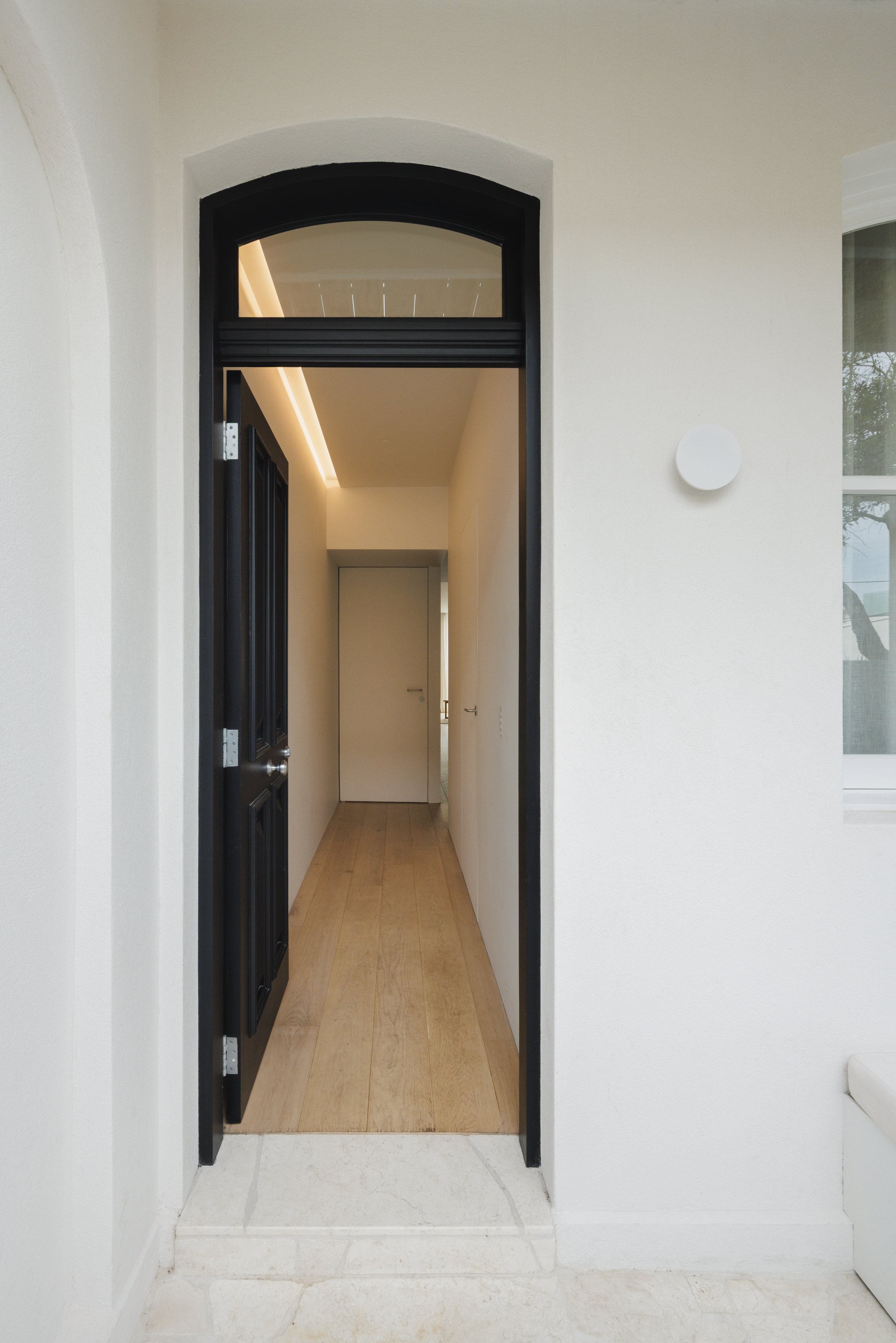 Detail view of an open front door, stone paving, timber flooring and soft lighting illuminating a corridor.
