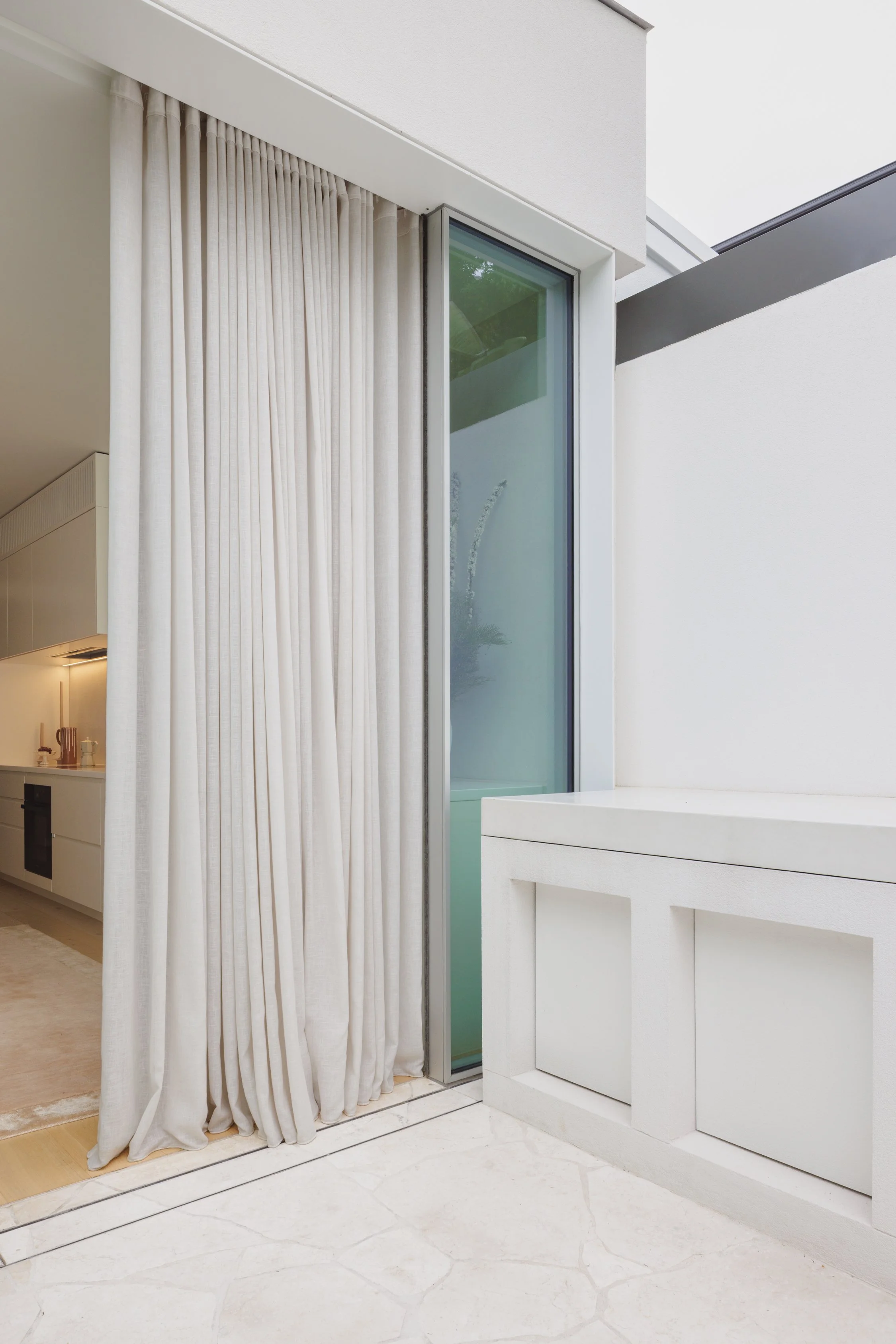 Modern facade with steel reveal, glazing, sheer curtains and textured walls and surfaces.