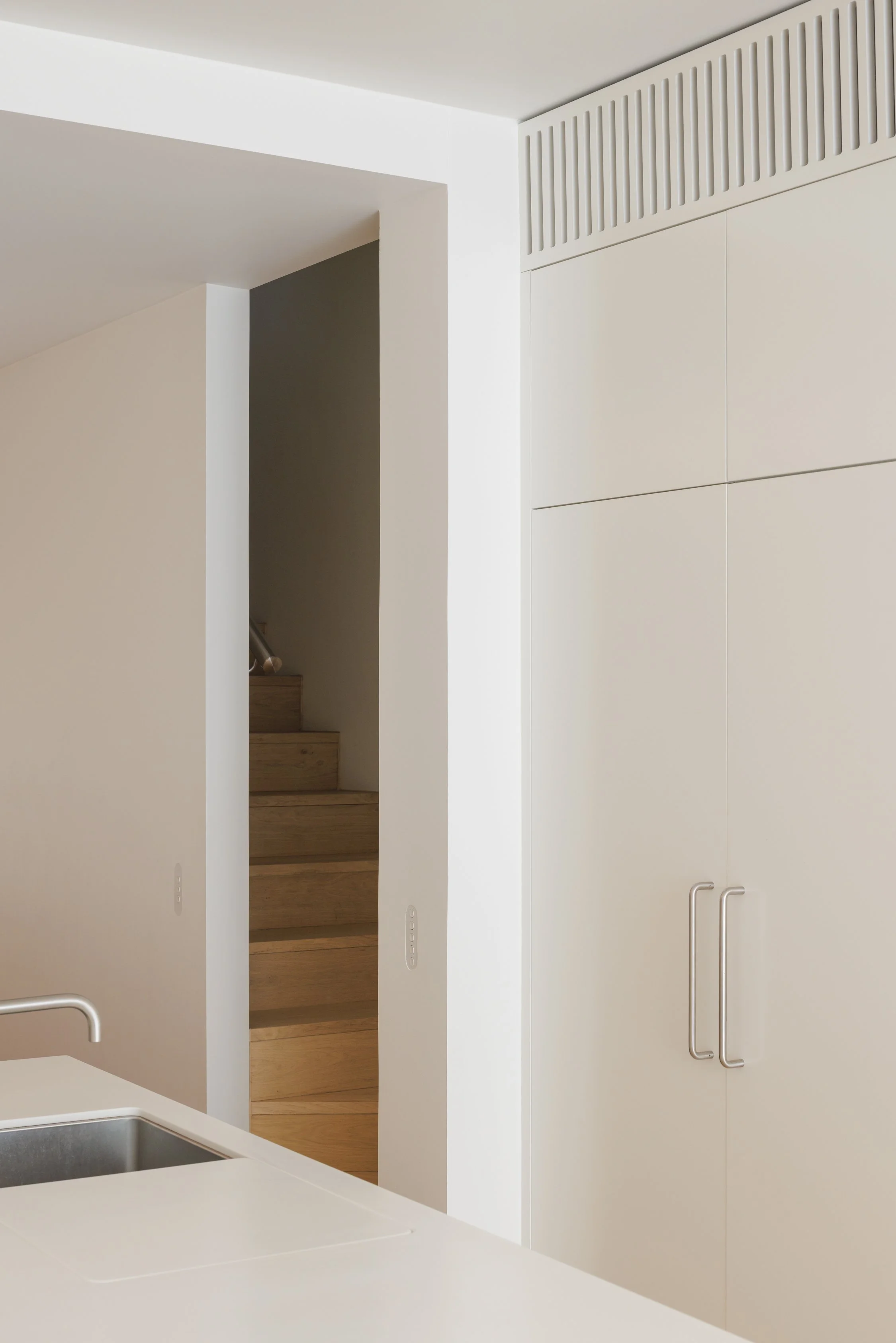 Detail view of a modern kitchen with custom cabinetry, stainless steel fixtures and fittings and timber stairs beyond.