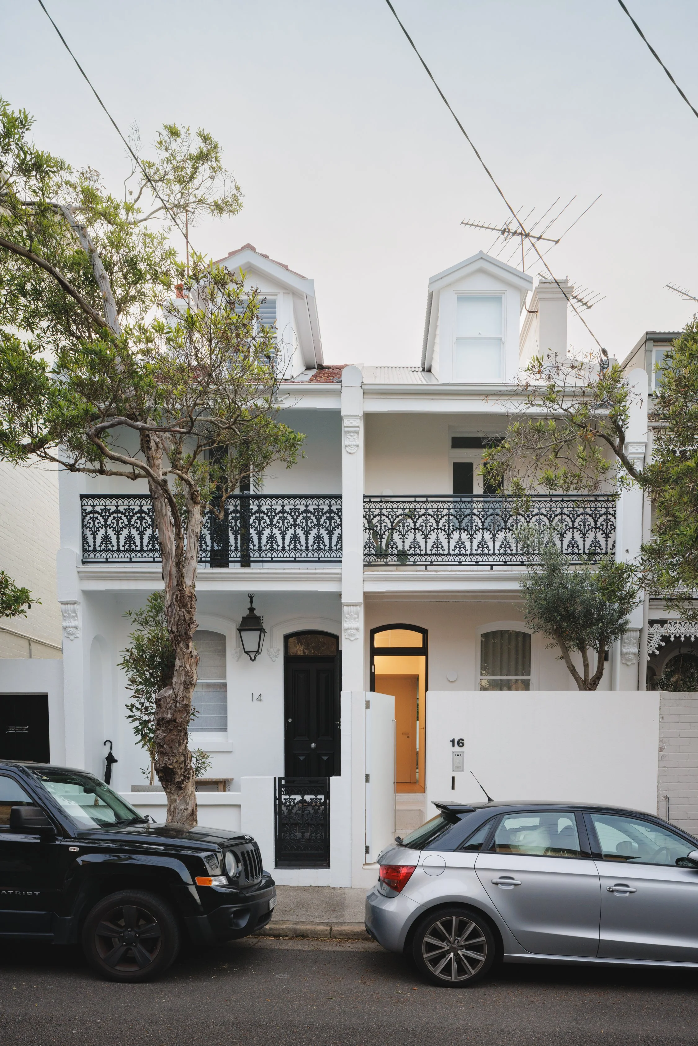 Street view of a multi-story terrace house with white textured walls, traditional timber windows and doors and soft lighting.