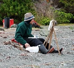 Thomas Arnatt plein air painting with an easel and art supplies, Gwaii Haanas, 2011. Photo DG Parks Canada (click for link to story)