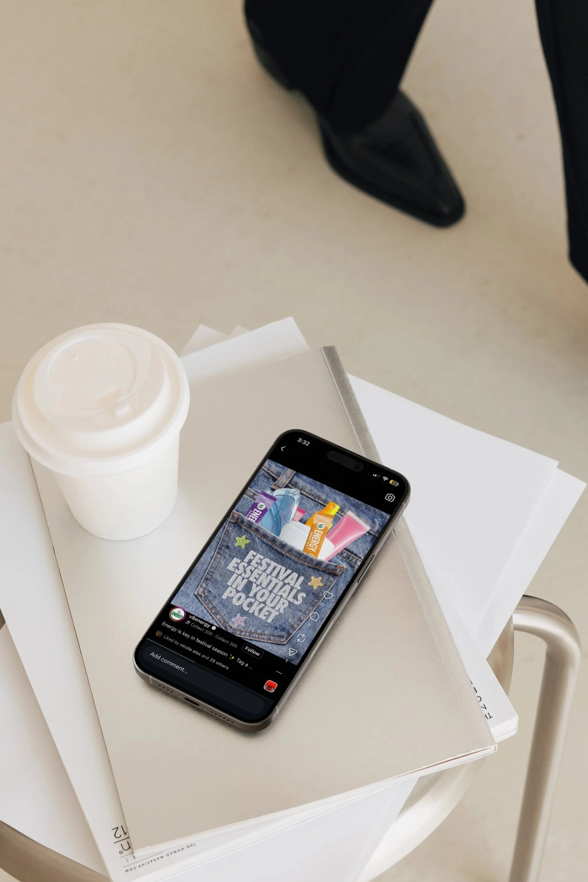 A white table with a white paper cup, a smartphone showing a picture of a denim pocket with a message, and a white box underneath the table.