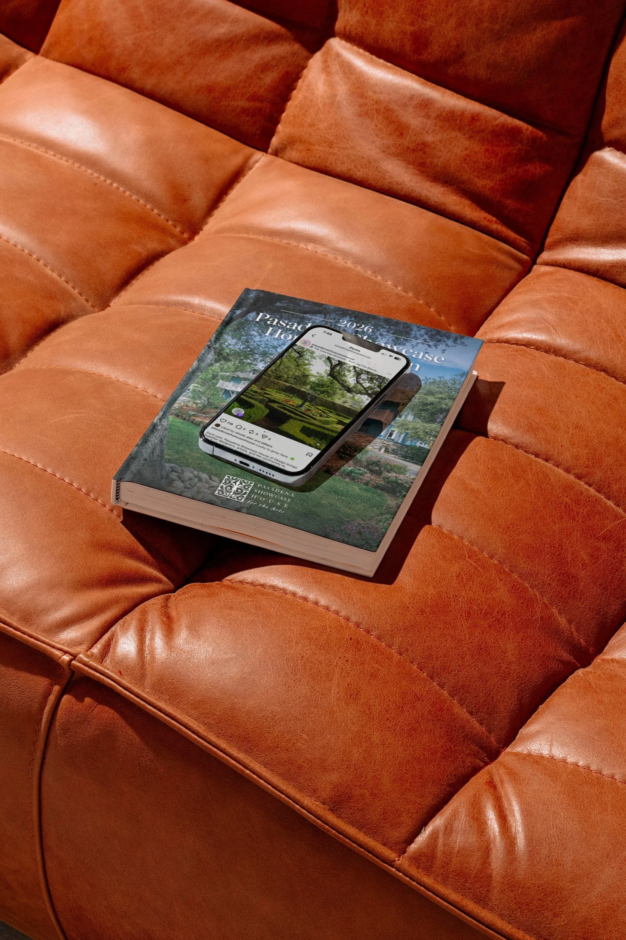 A brown leather couch with a book and a smartphone resting on it.