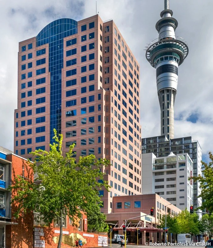 City view with tall skyscrapers, a communications tower, traffic lights, and trees in the foreground.